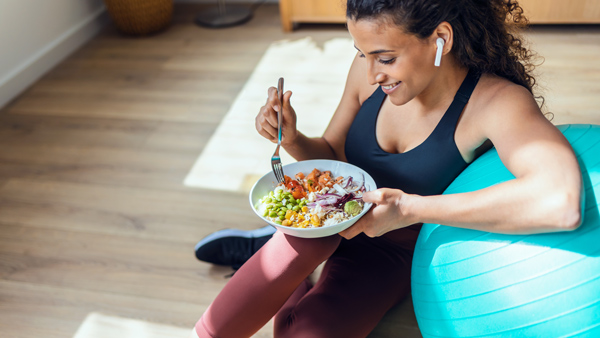 woman in workout gear eating salad against fitness ball