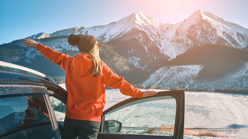 woman standing out of car door in winter gear looking at snowy mountains in view