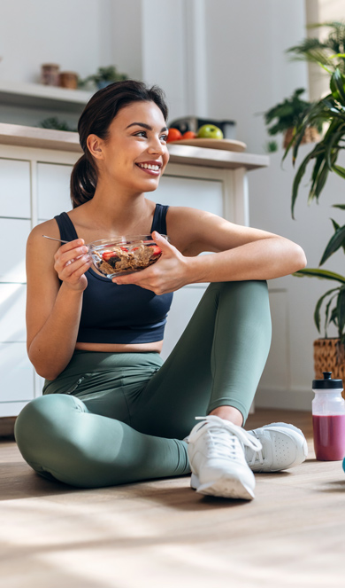 woman eating bowl of cereal after workout on floor, fitness gear