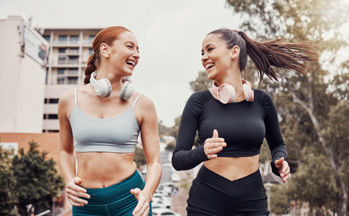 girls running outside together, laughing, headphones round neck